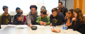 Instructor works with students at a table in the "Film on a Phone" classroom.