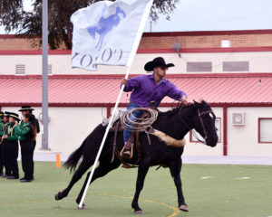 Photo of NMHU cowboy on a galloping horse and carrying the NMHU flag,