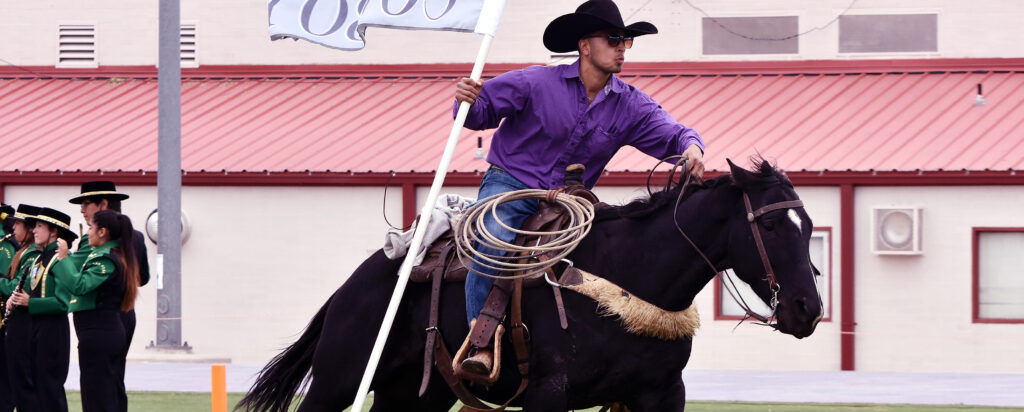 Photo of NMHU cowboy on a galloping horse and carrying the NMHU flag,