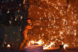 image of sparks flying as artist pours molten metal against a wall