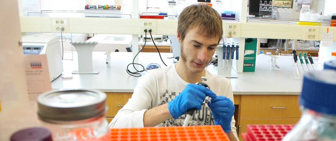 student working in biology lab holding an instrument.