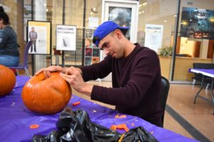 Photo of student at table carving a pumpkin.