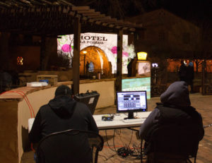 Photo of two students with computers viewing media projection on the wall of La Posada Hotel.