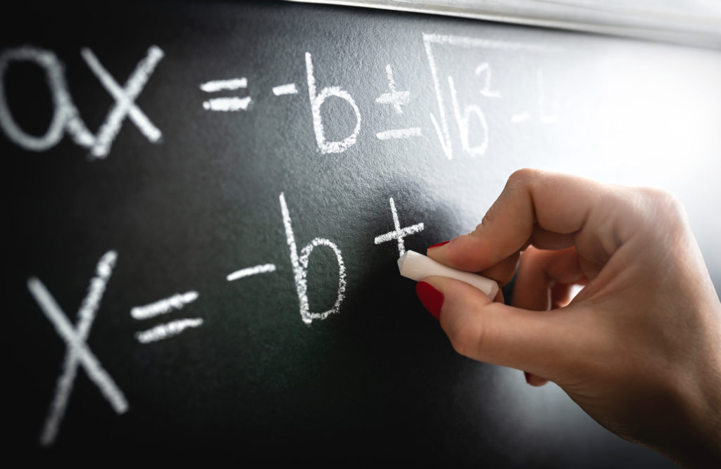 Close up of a hand with chalk writing a mathematical equation on a blackboard