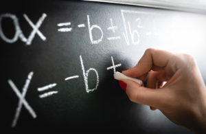 Close up of a hand with chalk writing a mathematical equation on a blackboard