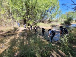 Students wearing backpacks walk through a forested area as a part of the STEM Showdown