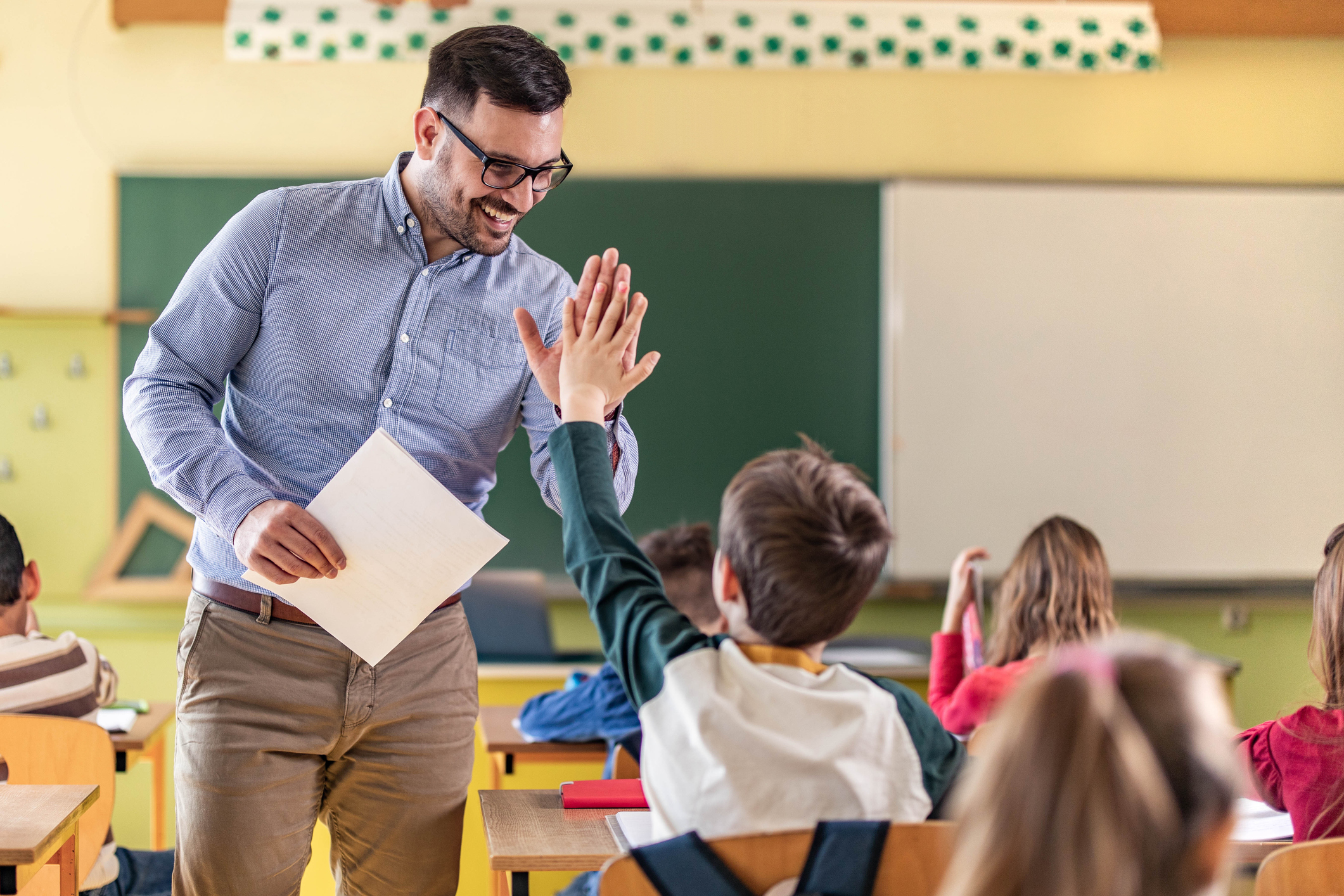 Happy male teacher giving high-five to his elementary student on a class in the classroom.