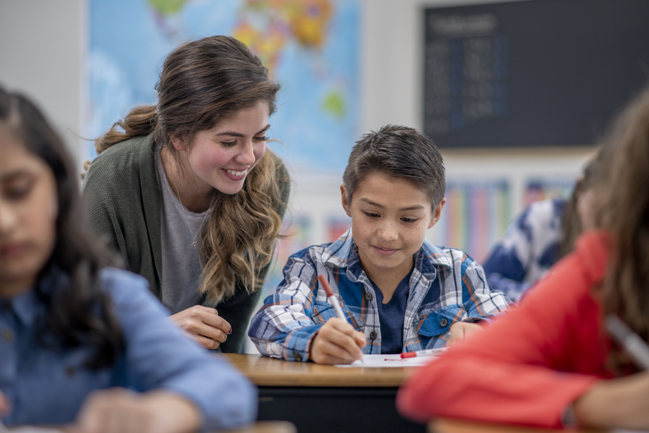 A Caucasian female elementary school teacher helps her student in her classroom.