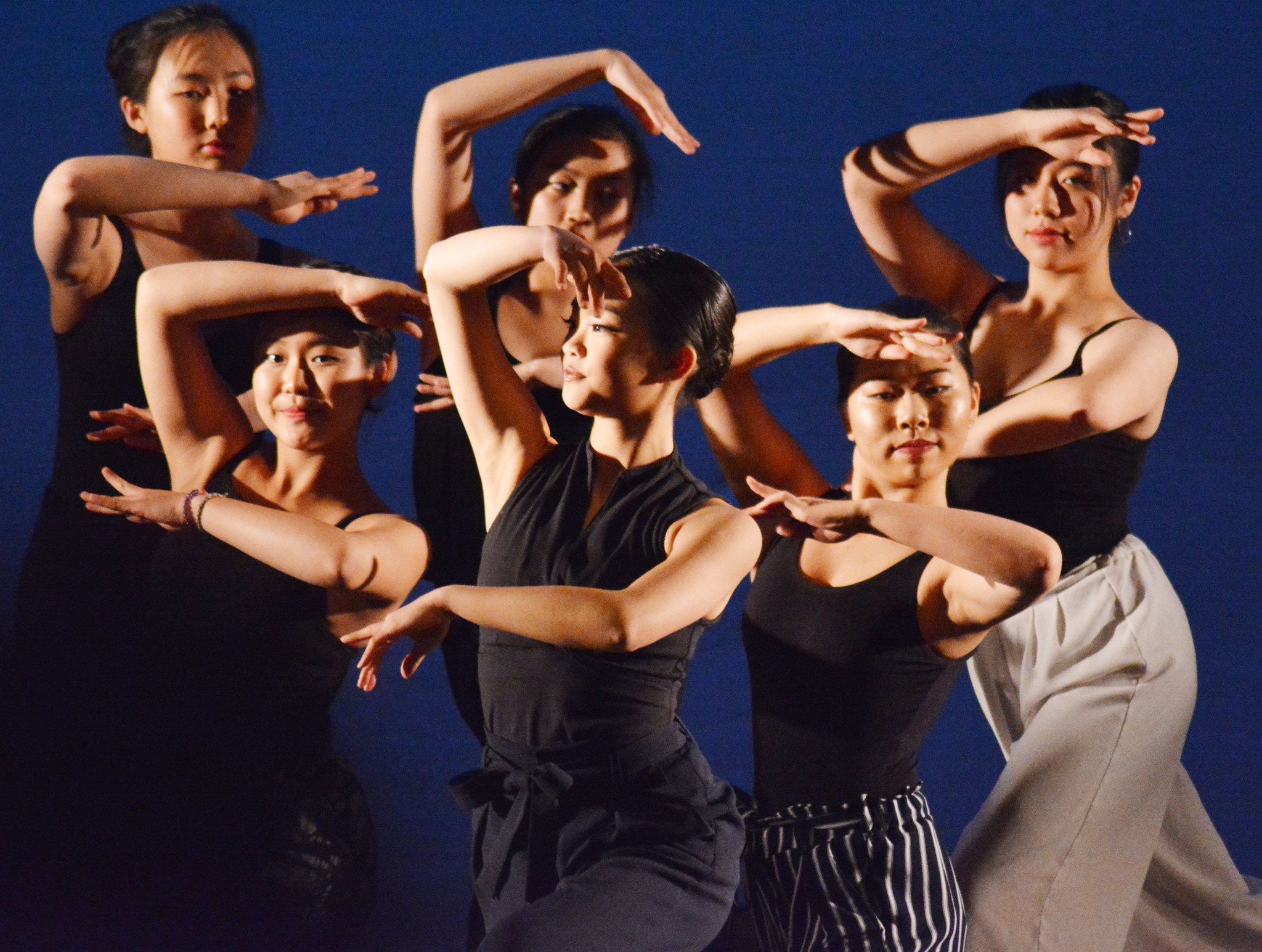 Photo of dancers with arched arms, silhouetted against a dark background