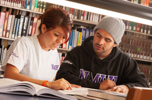 A latino male and latina female student are studying together at a table in the library.