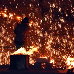 Silhouette of an artist working at a fiery forge as sparks fall from the ceiling.