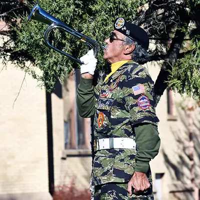 A man in uniform is outside playing a bugle.
