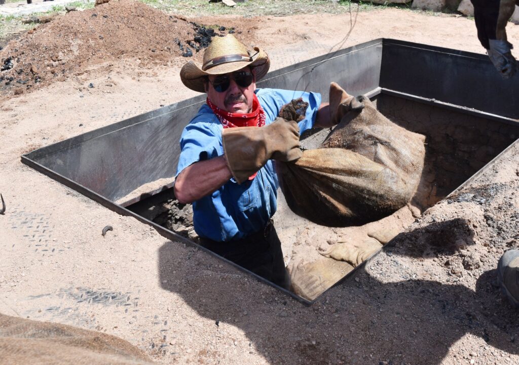 A man in a cowboy hat pulls a bag out from a pit in the ground.