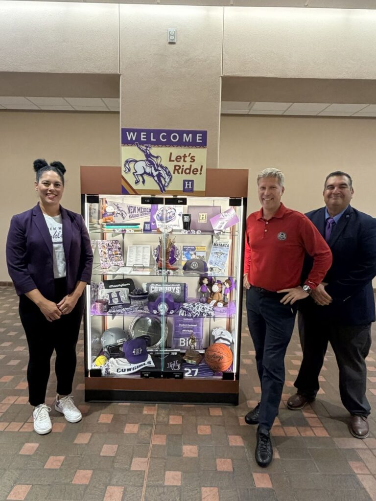 Three people standing at an NMHU display