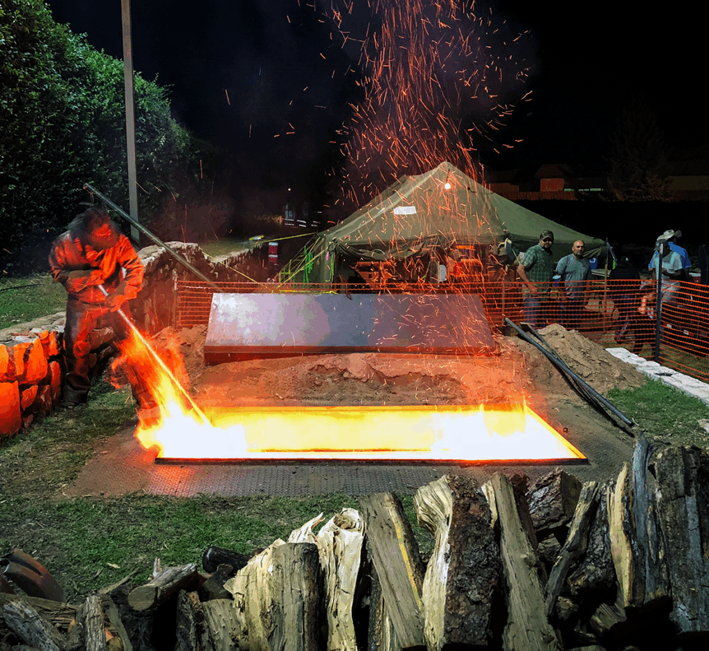 Image of a fire pit at night being stoked by a man in a cowboy hat.