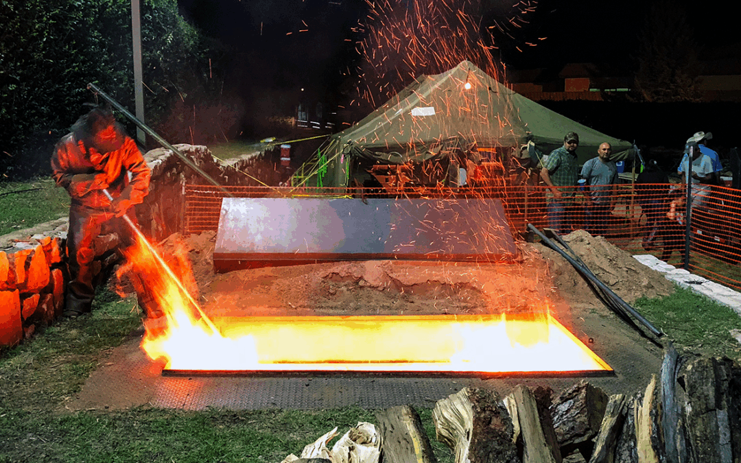 Image of a fire pit at night being stoked by a man in a cowboy hat.