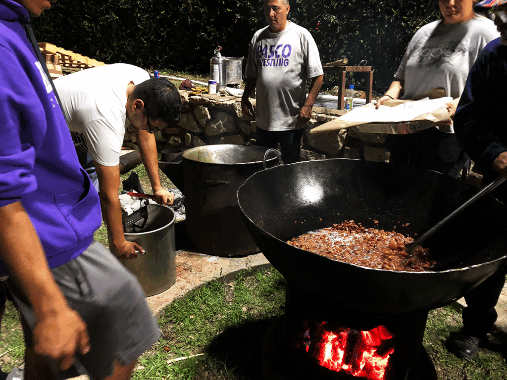 Image of people cooking with a large cast iron pot over a small fire.