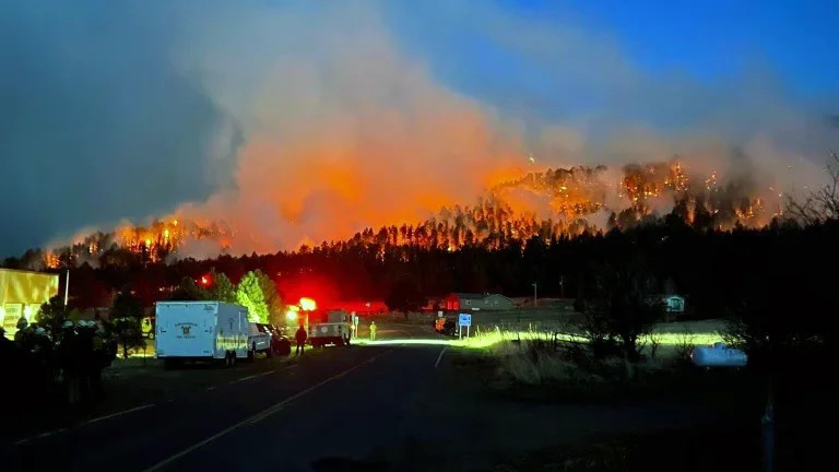 Image of the Hermit's Peak forest fire in the evening. Fire and rescue vehicles and equipment are seen in the foreground of the picture.