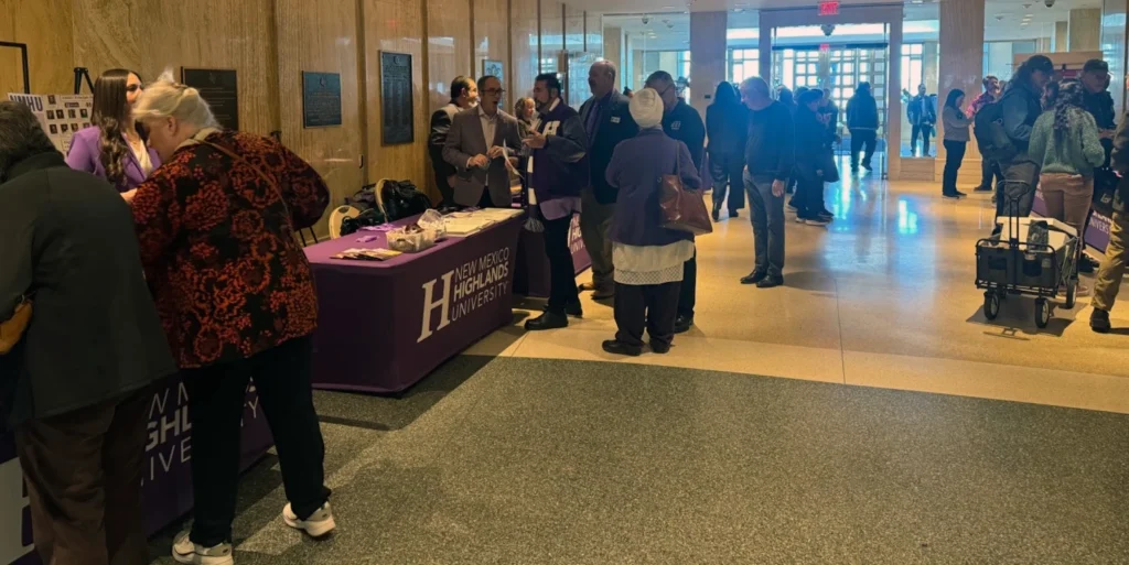 Image of people standing a a number of NMHU-branded tables during NMHU Day at the NM Legislature
