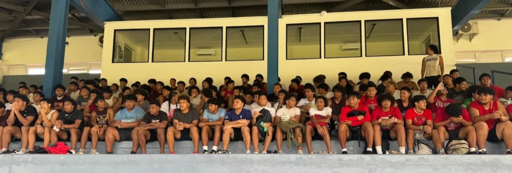 Image of student athletes in American Samoa sitting in the bleachers during instruction at football camp.