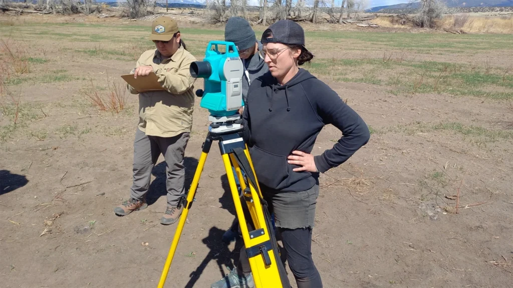 A female student conducting research, looking at the horizon through a measuring scope on a tripod.