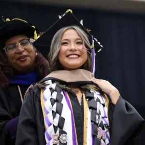 An image of a female latina Ph.D. student being hooded at a graduation ceremony.